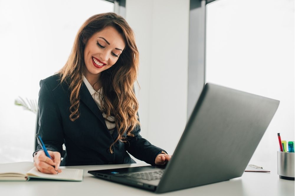 Woman writing in a notepad before a laptop